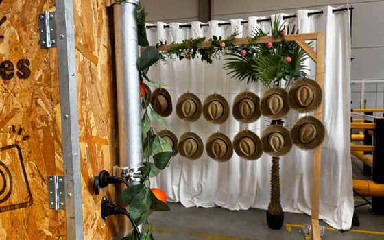 Coin photo installé pour un mariage : rideaux blancs, cadre doré et chapeaux de paille